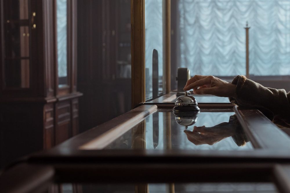 Hand pressing a brass service bell on a polished wooden desk