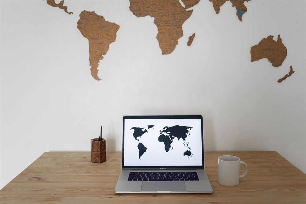 Laptop showing a world map on a tidy desk beside a coffee cup
