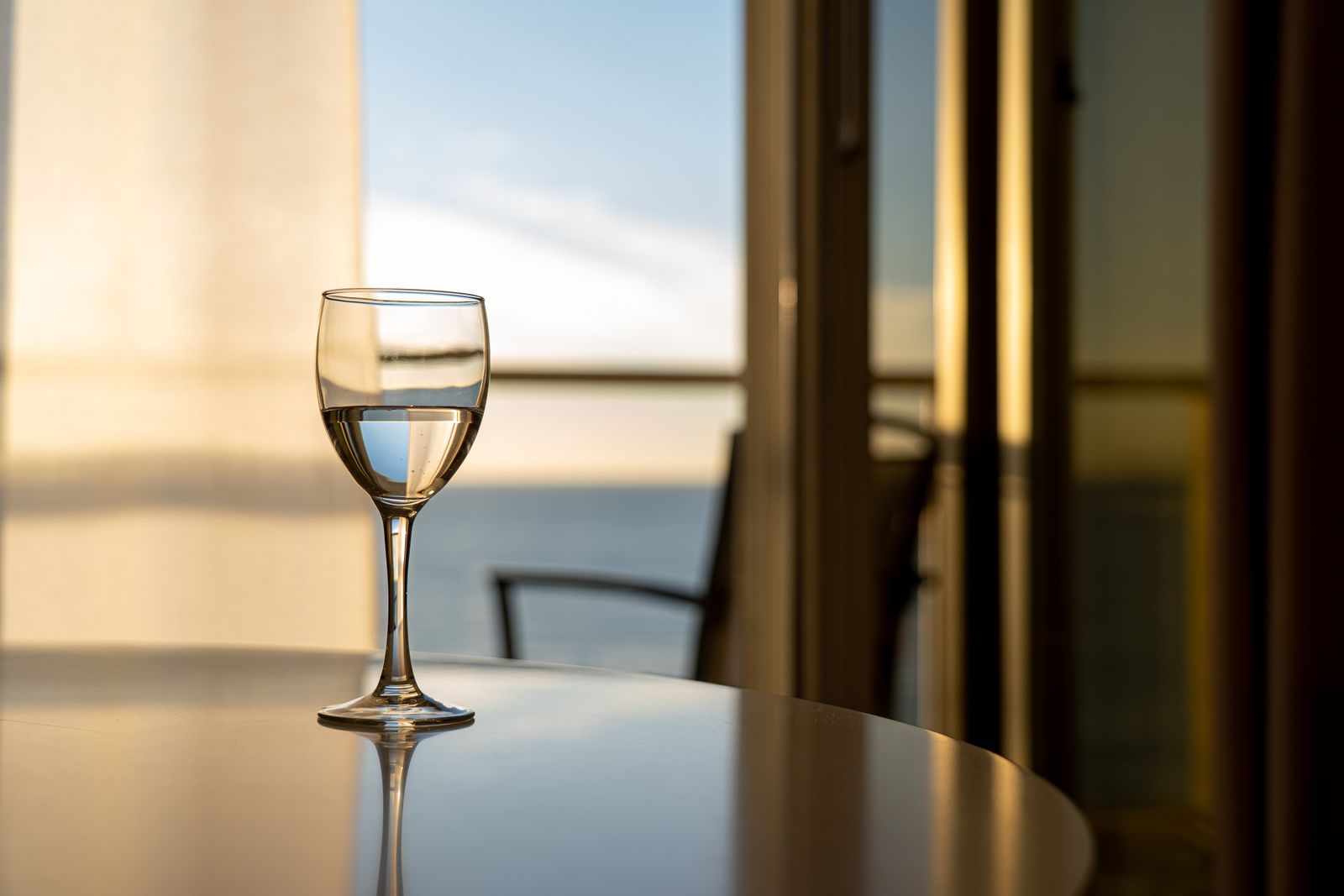 Glass of white wine on a table by a window looking out to sea
